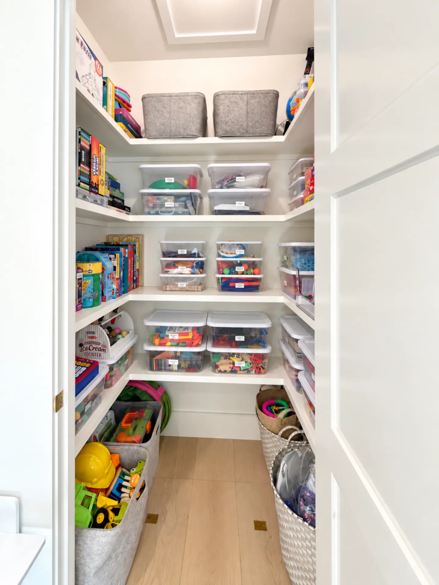 Organized playroom closet seen from the doorway, with floor bins of large toys along both walls