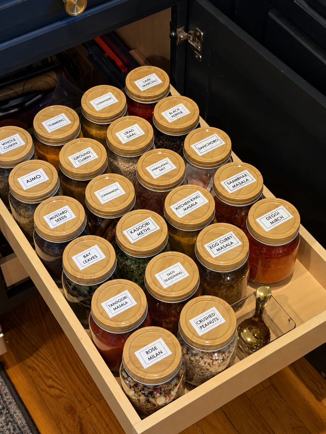 Pull-out drawer filled with uniform glass jars of spices and lentils with bamboo lids and white labels, viewed from above