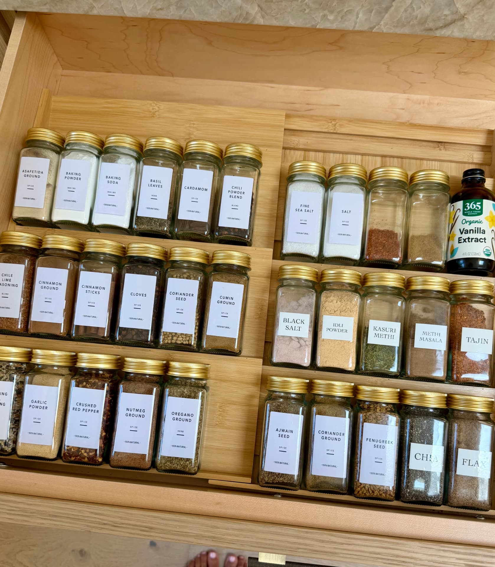 Two-tier bamboo spice drawer with labeled jars of spices and extracts with gold lids